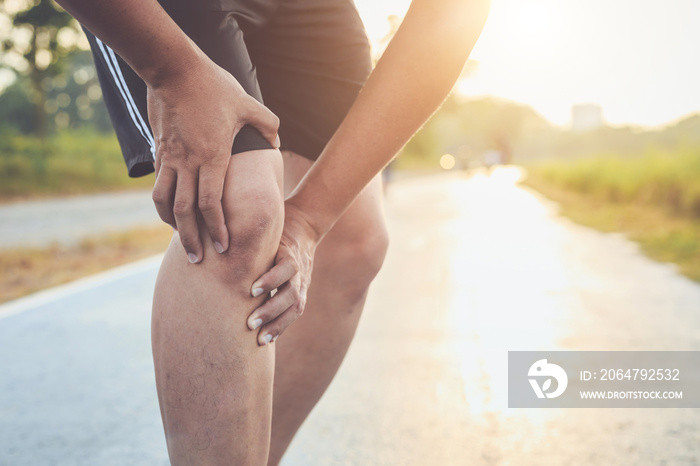锻炼概念造成的伤害：一名亚洲男子在公园的路上跑步时用手抓住膝盖