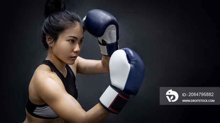 Young Asian woman boxer posing uppercut with blue boxing gloves in fitness gym. Female boxing class.