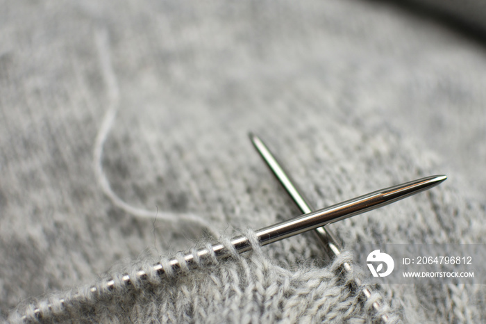 Place for an inscription.  Knitting. Gray knitted fabric on steel knitting needles. Close-up.