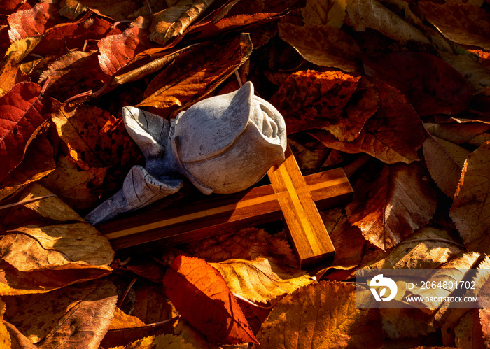 Eine Rose aus Stein mit Holzkreuz zum Abschied im Herbstlaub.