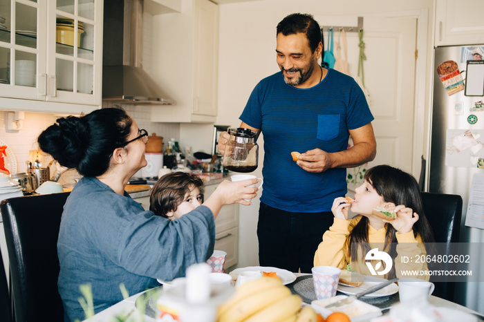 Man serving coffee to woman sitting with children at dining table