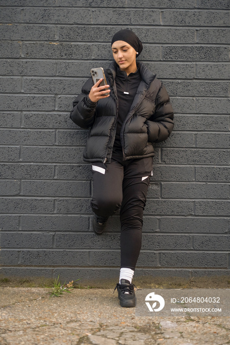 Young woman leaning on wall and using smartphone