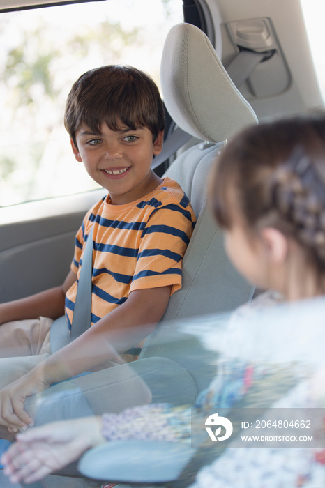 Happy brother and sister riding in backseat of car