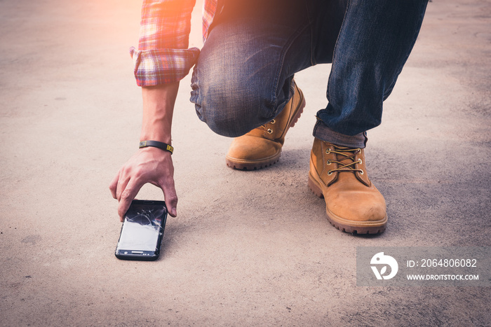 the abstract image of the man picking a broken smartphone up from sement floor. the concept of broke