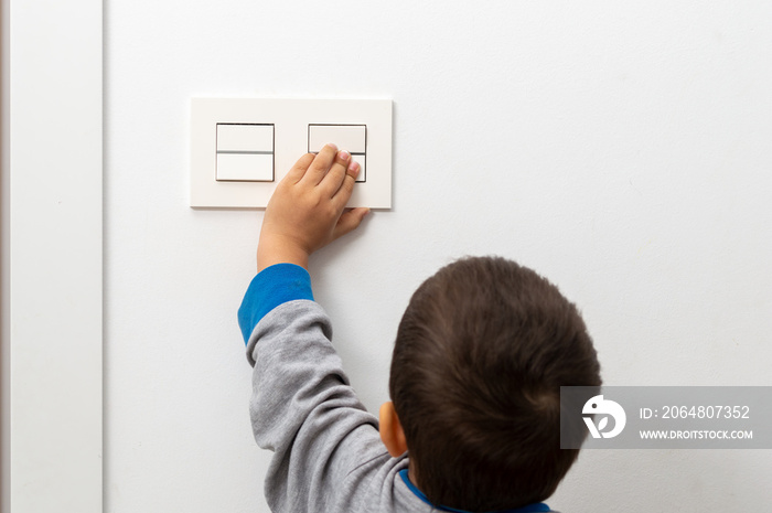 一个粗心的小男孩在探索房子时玩电灯开关的后视图，家用电器