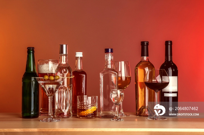 Table with different bottles of wine and spirits on color background