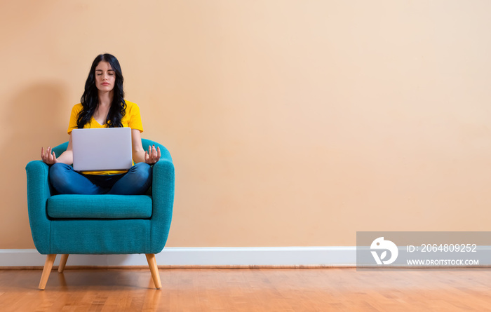 Young woman with laptop in a meditation pose pose sitting in a chair