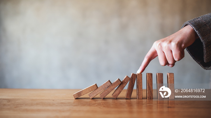 Closeup image of a finger try to stopping falling wooden dominoes blocks for business solution conce