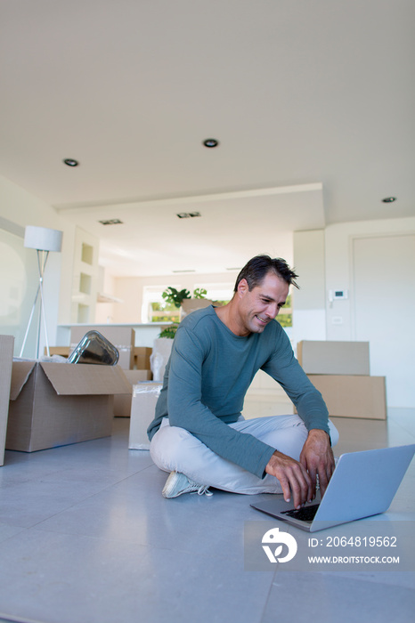 Man using laptop on floor with moving boxes in new house