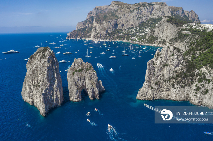 Aerial drone shot view of faraglioni limestone crags in summer in Tyrrhenian sea with yachts off Cap