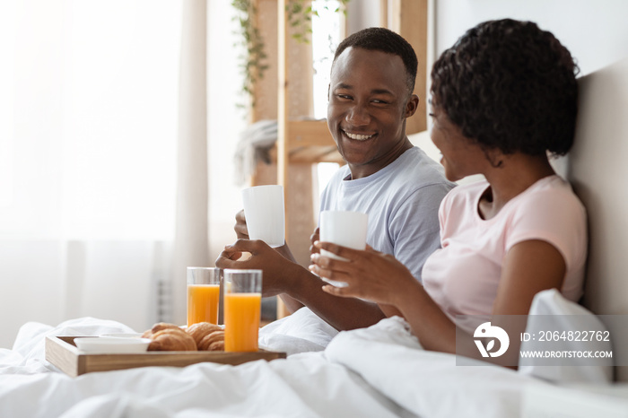 Happy young black couple eating breakfast in bed in morning