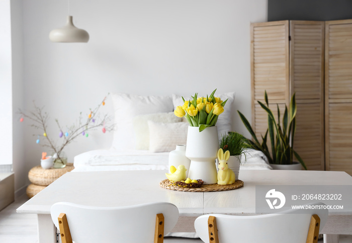 Vase with tulips, Easter eggs and decor on dining table in light room interior