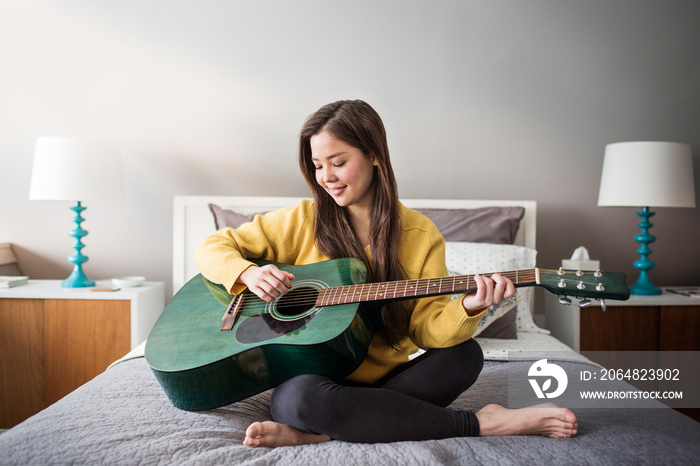 Young woman playing guitar in bedroom