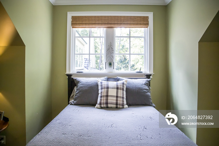 A bedroom with green walls and gray bedding and a plaid pillow with a window behind the bed