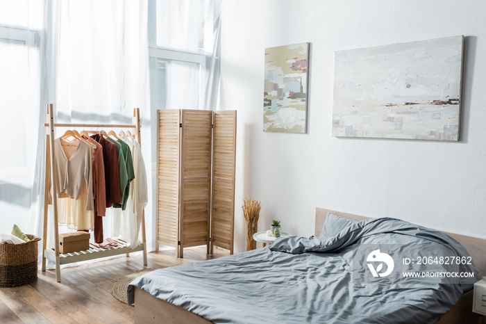 modern bed near folding screen and rack with clothes in bedroom.