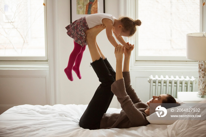 Side view of playful mother picking up daughter while lying on bed at home