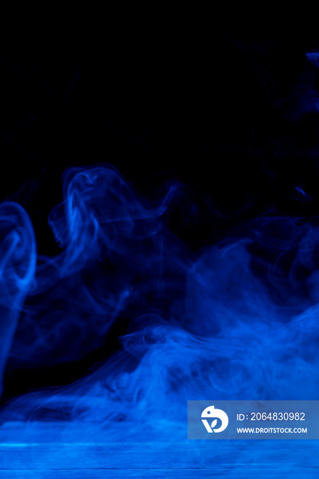 深黑色背景和木制桌子上孤立的蓝色烟雾概念图。