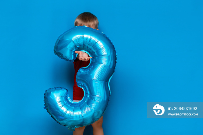 small cute blonde boy on blue background holding foil-coated sphere baloon blue colour. happy birthd