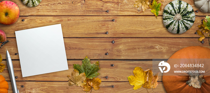 Autumn decoration with fallen leaves, pumpkin, notepad and a pen on wooden background