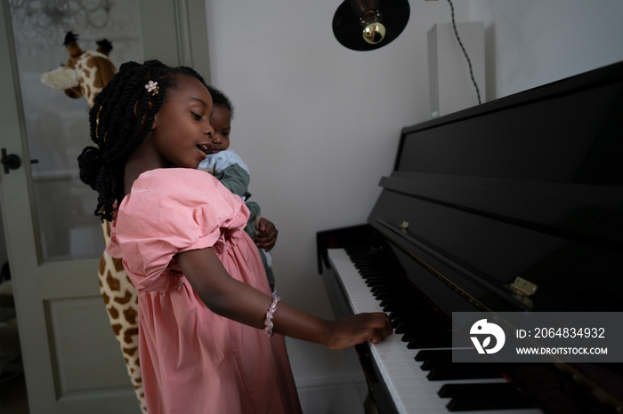 Girl (6-7) holding baby brother (2-5 months) and playing piano