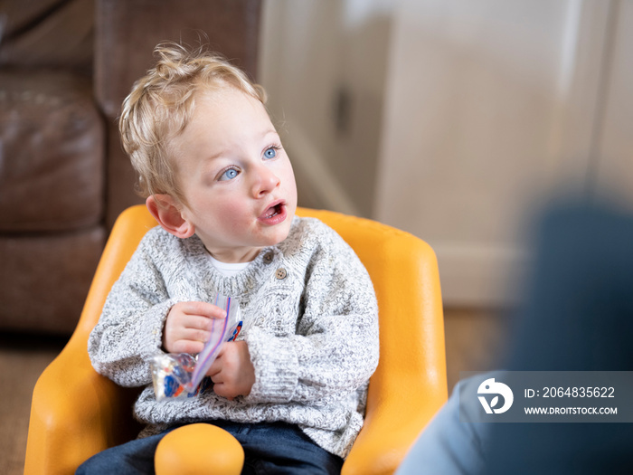 Blond boy in baby seat holding plastic bag�