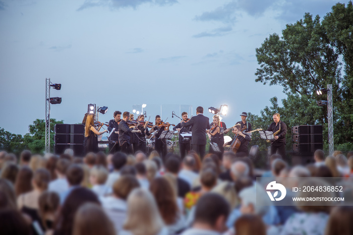 Orchestra performing live concert for audience under blue sky