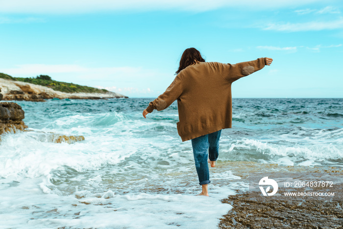 woman walking by rocky sea beach at sunny windy day. summer vacation