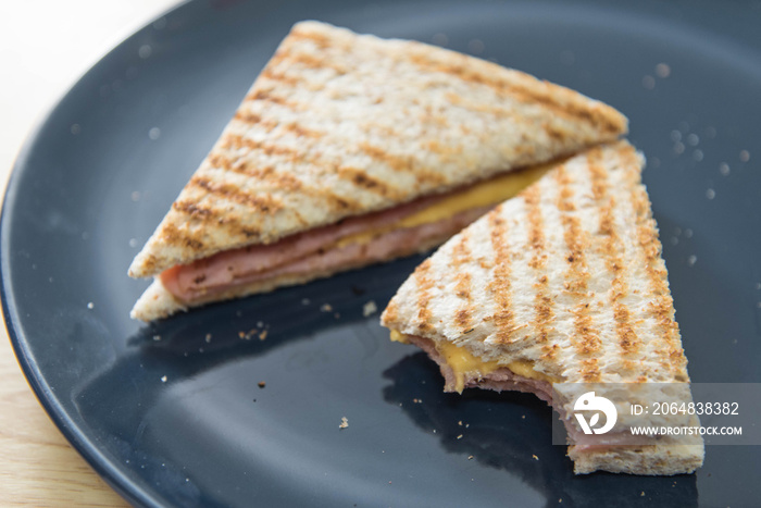 A half-eaten grilled ham and cheese sandwich on a blue plate