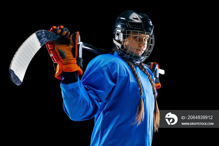 Young female hockey player isolated on black background. Sportswoman wearing equipment and helmet st