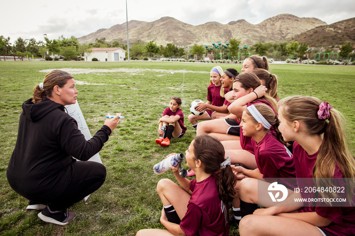 Mature female coach interacting with girls in sports uniform while making plan on whiteboard during 