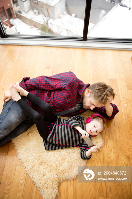 Father and daughter listening to music while lying on rug at home