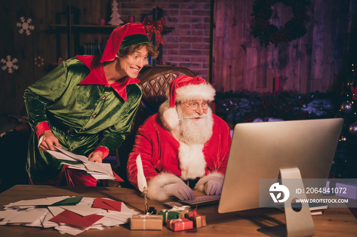 Photo portrait of santa claus and elf looking at computer screen holding bunch of letters