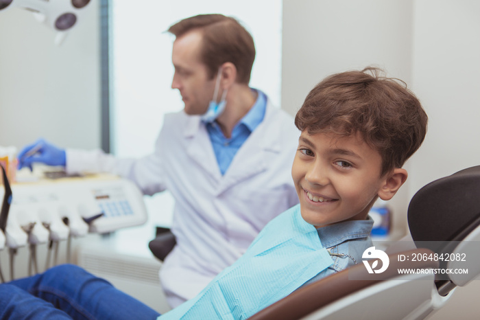 Childrens dentistry. Lovely cheerful boy smiling to the camera, waiting for dental checkup by his or