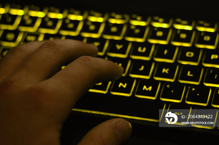 Mans hand typing on keyboard with yellow backlight