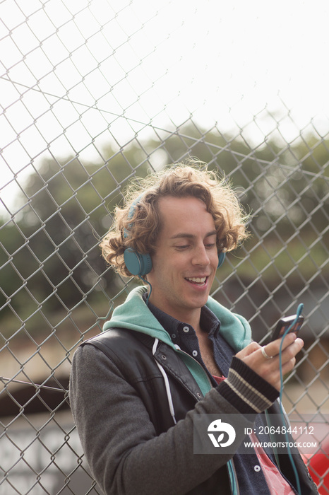 Man with headphones and smart phone listening to music at fence