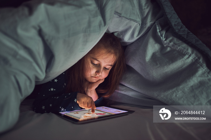 Little girl having fun watching, playing and listening to stories on tablet computer. Child having f