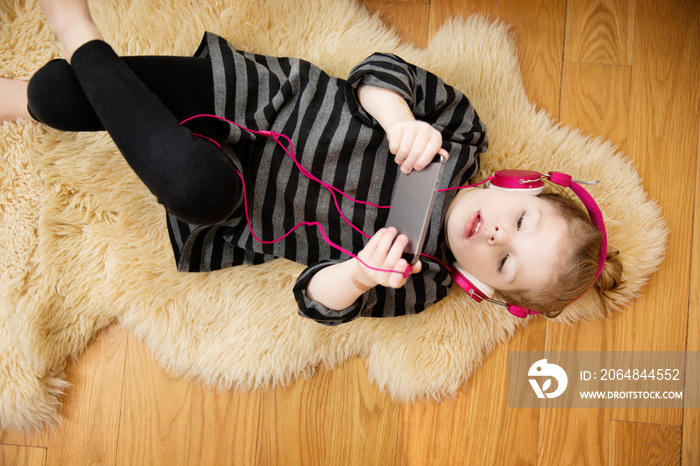 Girl (4-5) lying on rug listening to music