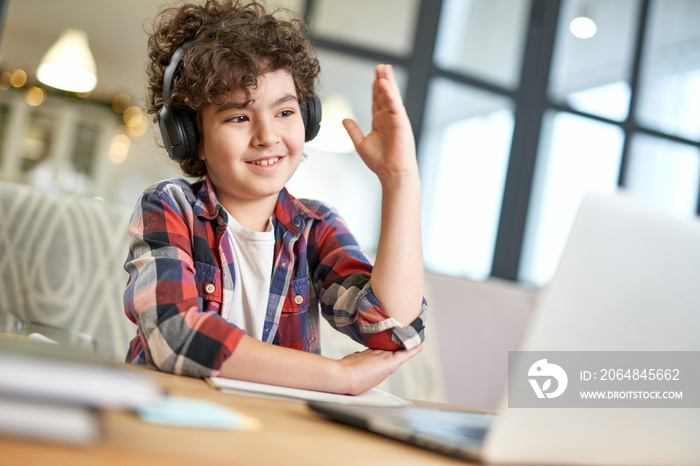 Curious latin american little boy wearing headphones, using laptop while studying at home. School ki