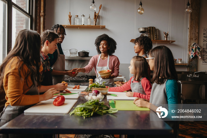 Female chef giving vegetables to students at table against wall in cooking class