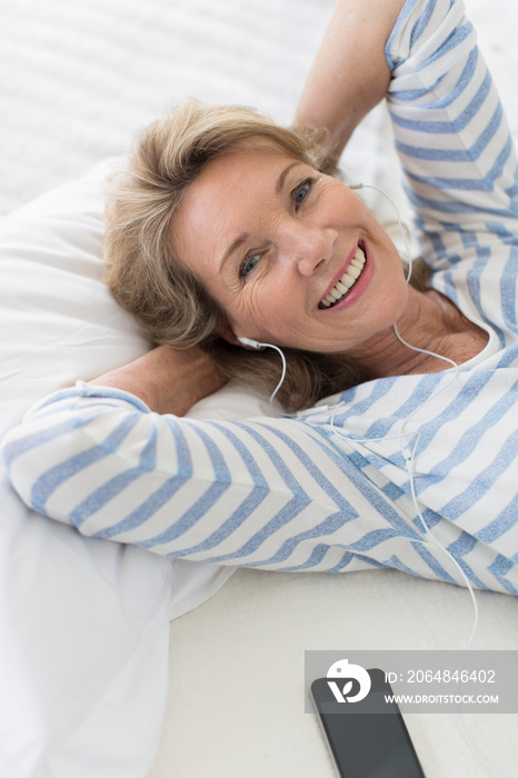Portrait happy senior woman listening to music with headphones on bed