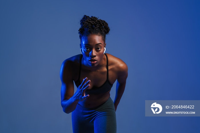 Black sportswoman in earphones doing exercise while working out