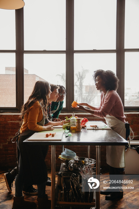 Side view of female chef explaining to students at table against windows in cooking class