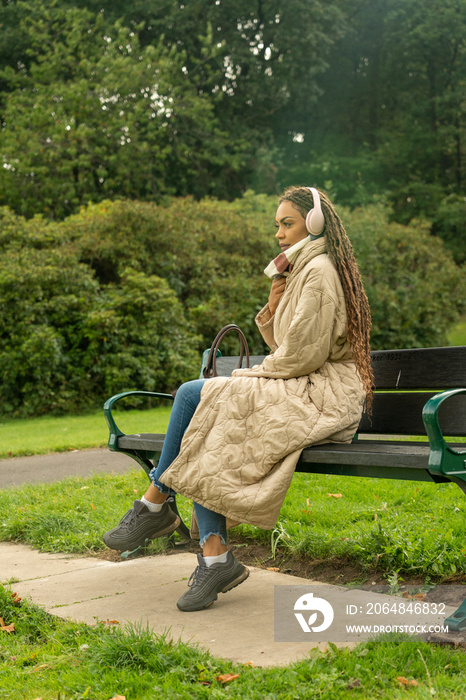 秋天公园里坐在长椅上戴着耳机的女人
