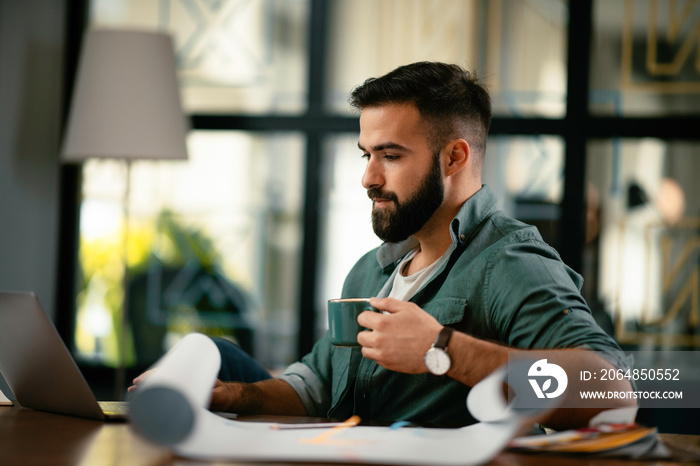 Handsome man drinking coffe in office. Young man working on project.