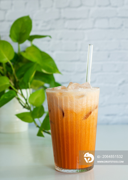 a glass of thai tea with milk on the white table with green leaf.