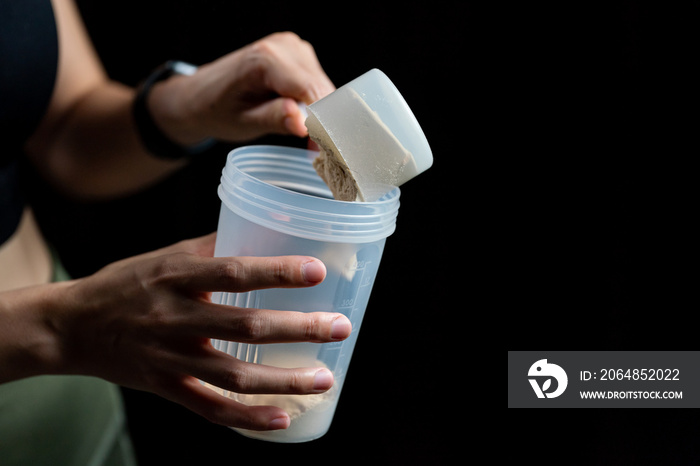 Close up of women with measuring scoop of whey protein and shaker bottle, preparing protein shake.