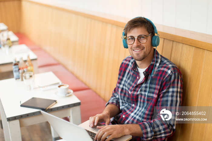 Portrait smiling man with headphones working at laptop in cafe