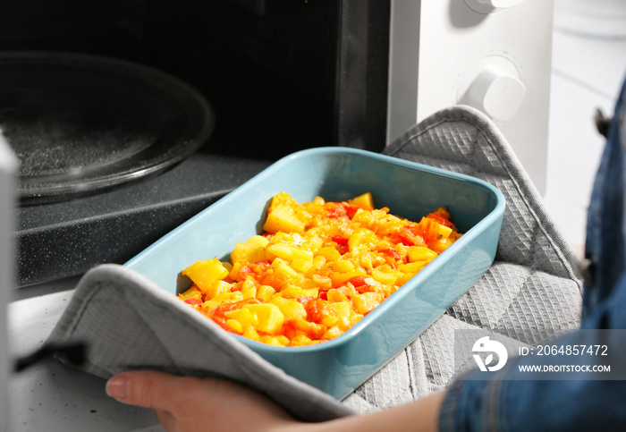 Woman taking out baking dish with dinner from microwave oven. Cooking for one concept