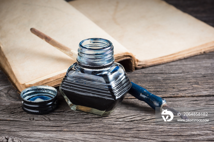 still life photography : inkwell with quill pen on old wood with opening old book at the back