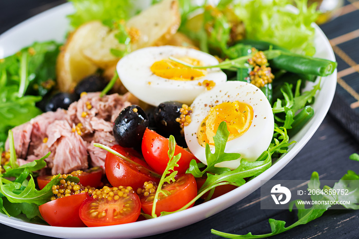 Healthy hearty salad of tuna, green beans, tomatoes, eggs, potatoes, black olives close-up in a bowl